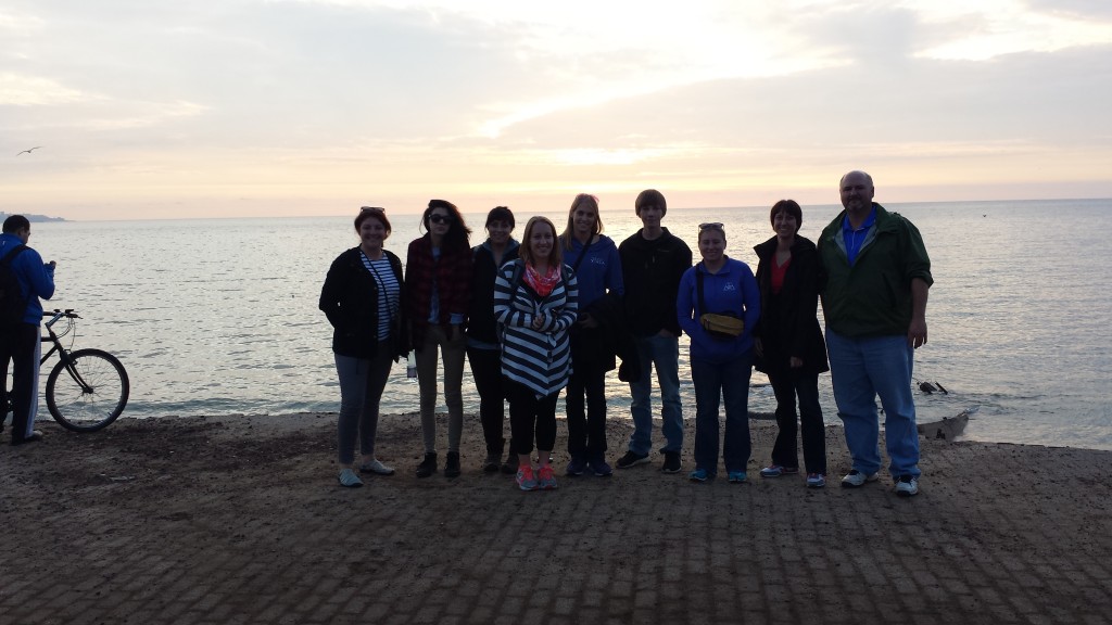 Group of UW students posing in front of the sunset on the Pacific Ocean.