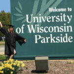 A graduation photo of Susan Suchy standing in front of a UW-Parkside sign.