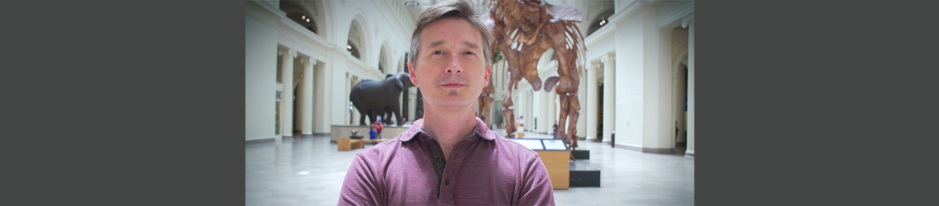 A photo of Carter O'Brien standing in front of a dinosaur skeleton at the Field Museum in Chicago.