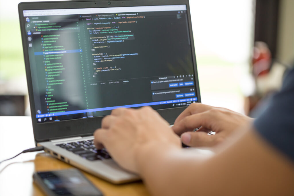 Person typing on keyboard of laptop with coding on the screen