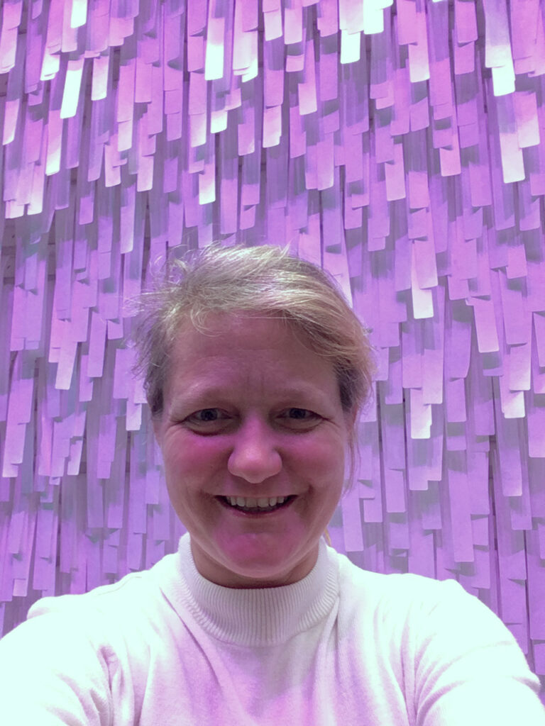 Sheilah Fondren smiling and posing in from of a purple art installation.