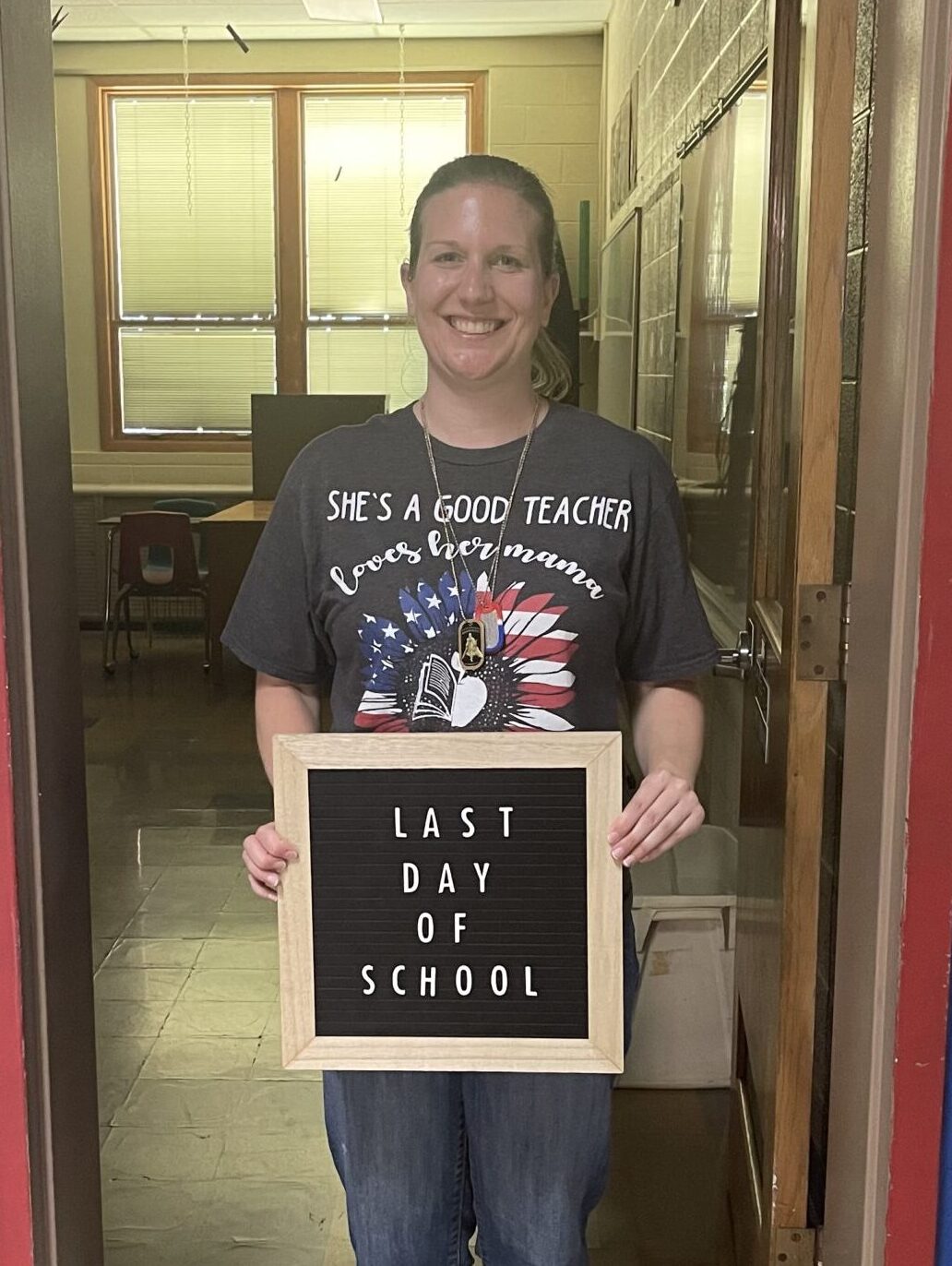 Sierra Erdmann holding a sign that says "Last Day of School" while standing in front of her classroom.