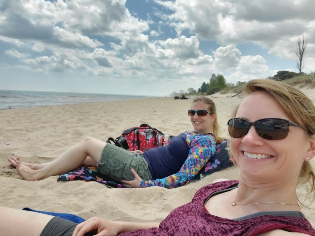 Sierra Erdmann and her friend laying down in the sand at a beach with clouds in the sky. 