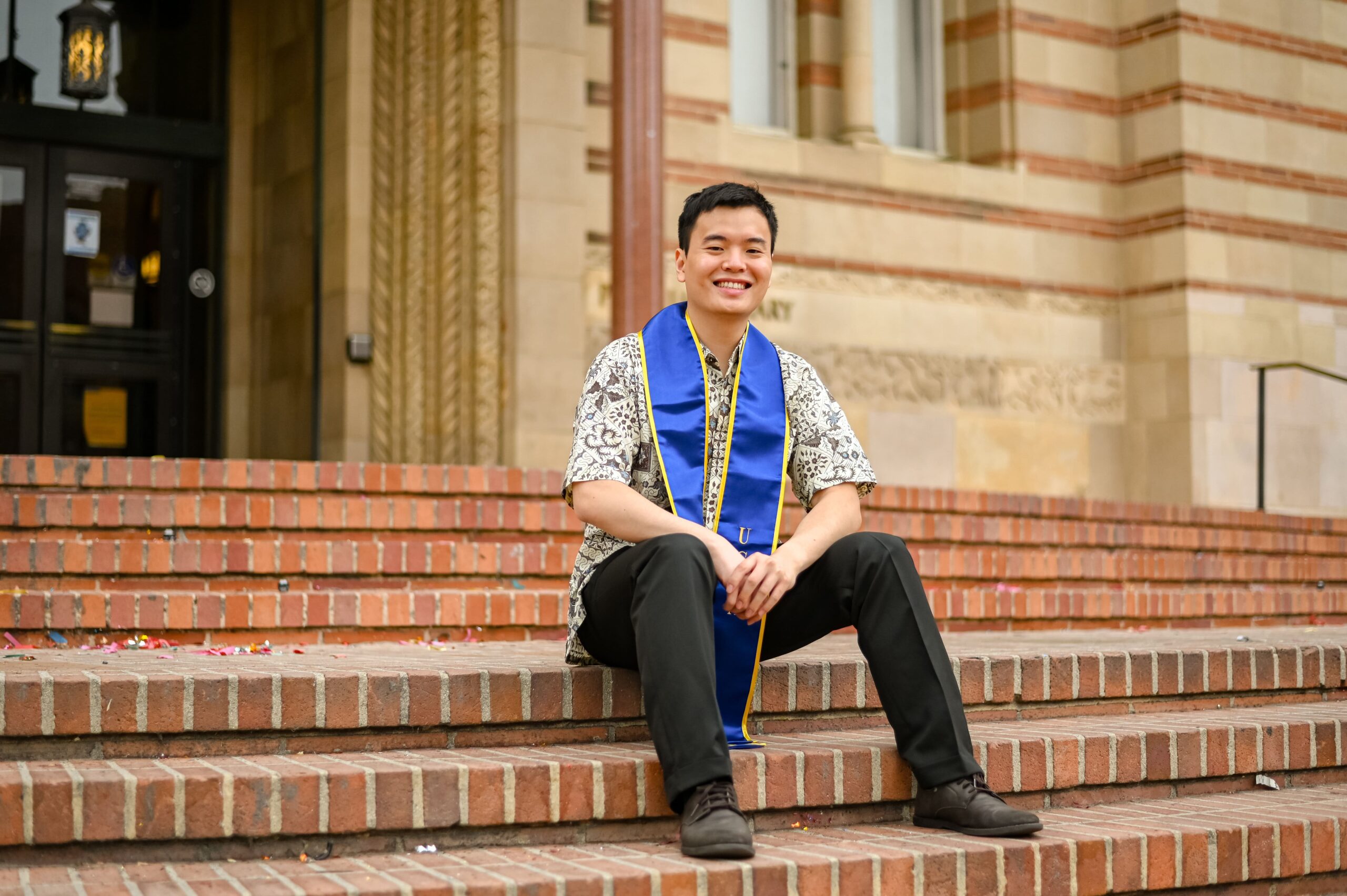 Jason sitting down on a set of stairs and wearing a stole in honor of his graduation from the University of California, Los Angeles.