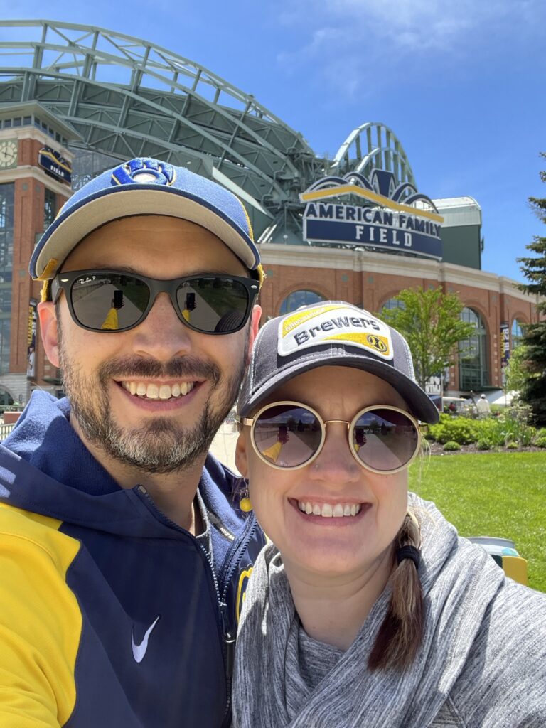 Michael Paul standing with his wife outside American Family Field and wearing Milwaukee Brewers gear. 
