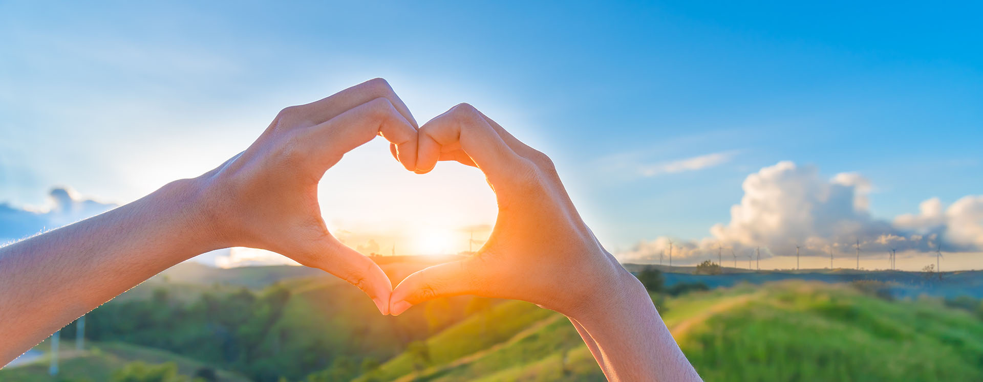 two hands making a heart shape with an outdoor background