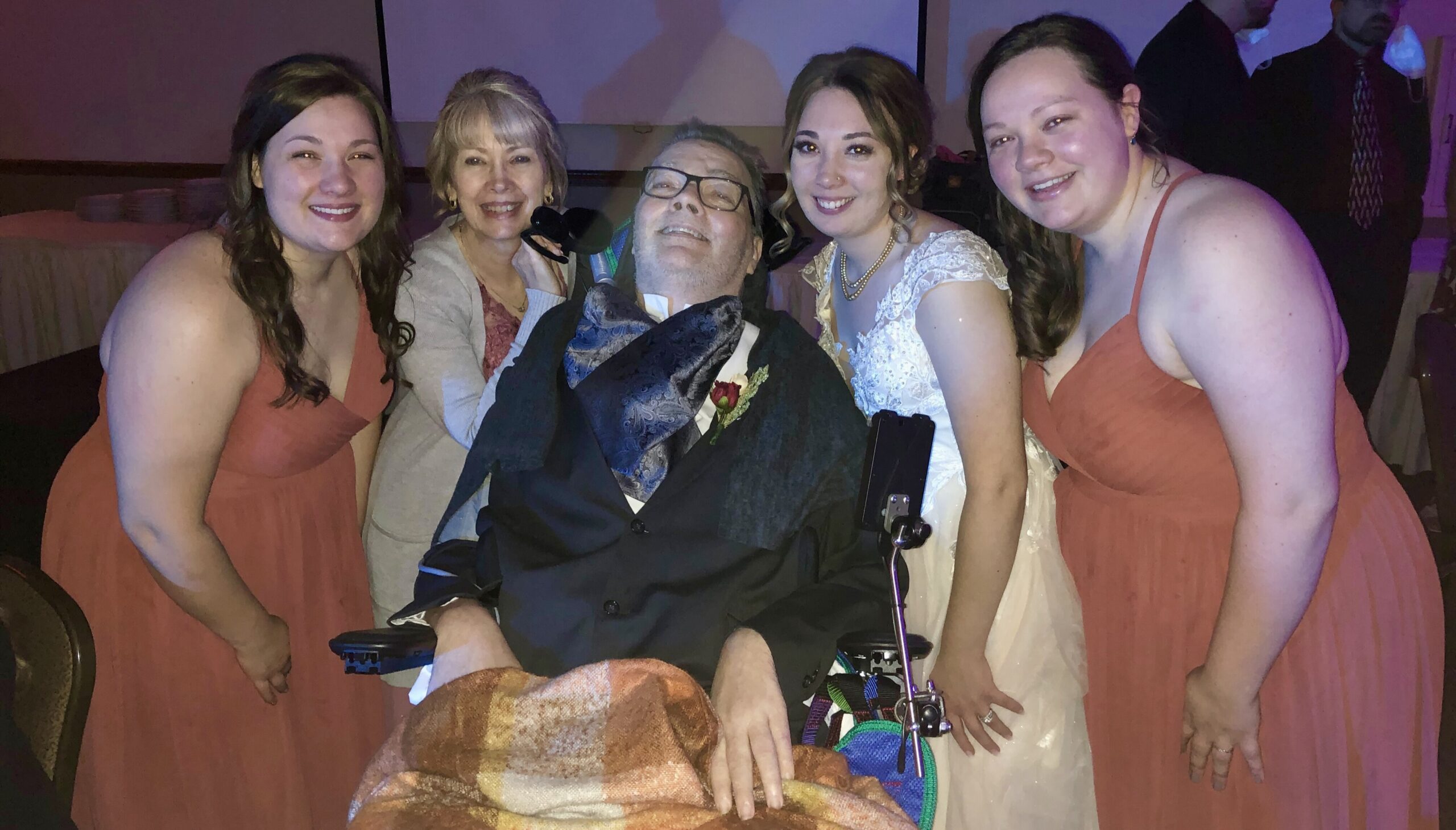 Britni wears a dress and is smiling as she poses with her family at a wedding. 