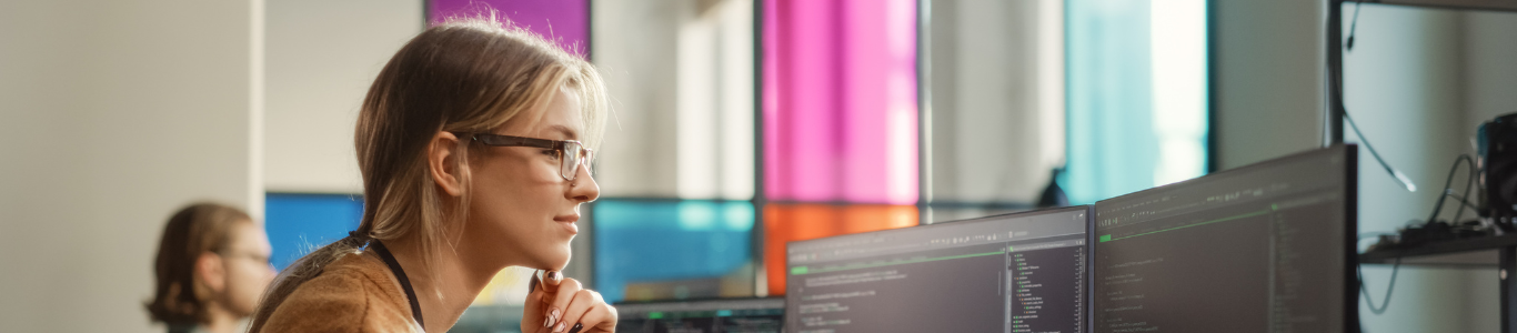 A blonde woman with glasses using a computer with two monitors. The UW Data Science program has updated its data science curriculum.