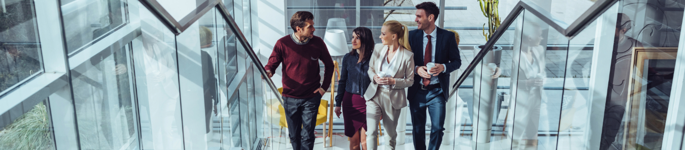 Four working professionals climb up an escalator at work