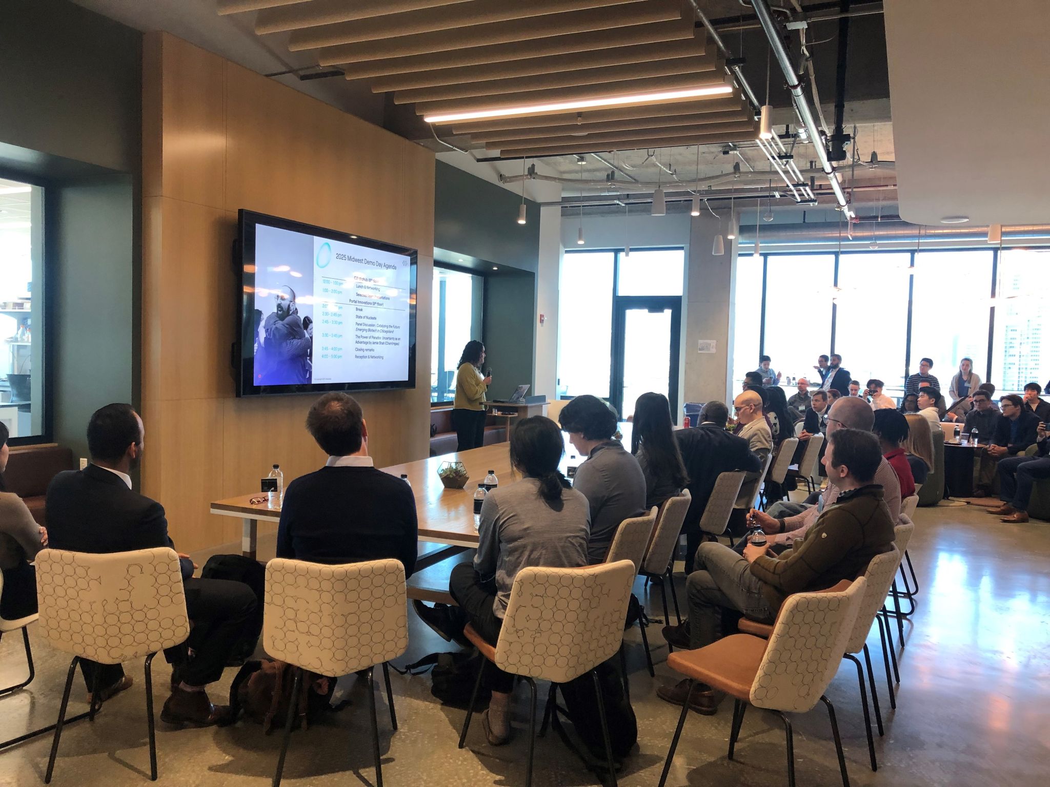 A group of people sit in chairs around a table as they watch a presentation during the Nucleate Midwest Demo Day, which Applied Biotechnology student Paul Luna attended. 