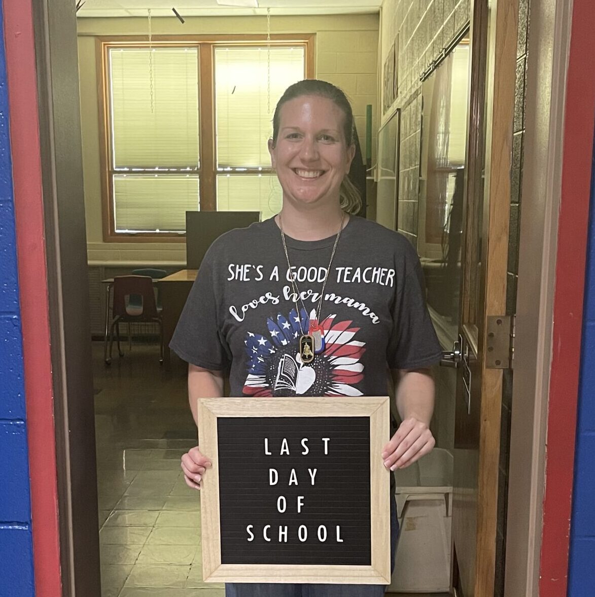 Data Science graduate Sierra Erdmann standing in a doorway holding a sign that reads 'Last Day of School' inside a school building.