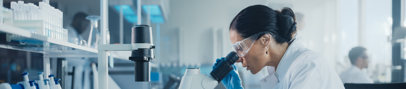 Female scientist looks under a microscope and analyzes a petri dish in a laboratory.