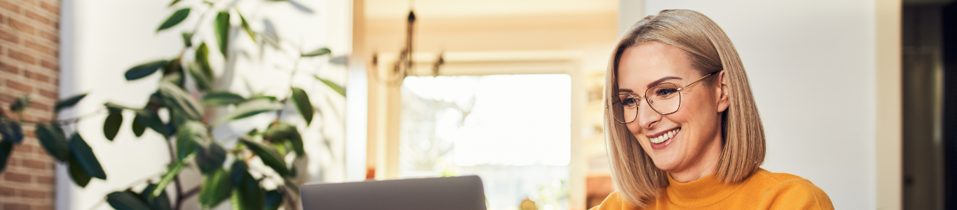 A woman smiles while using a laptop in her living room